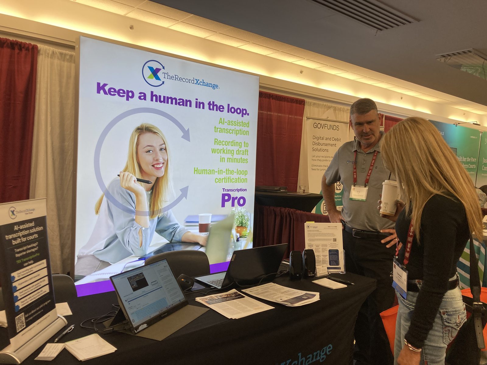 A conversation at the TheRecordXchange booth at NACM 2026, with the TRX TranscriptionPro banner and a laptop showing the software
